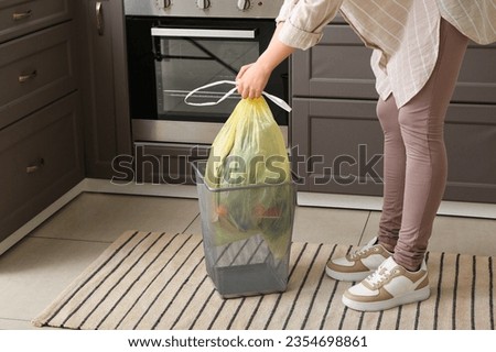 Woman taking full garbage bag from trash bin in kitchen Royalty-Free Stock Photo #2354698861