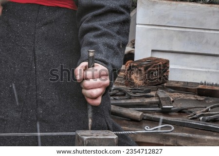 Close-up of authentic blacksmith working with hammer and iron at anvil of workshop. Traditional manually forging of molten metal. Craftsman worker forges iron detail creation