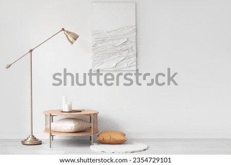 Wooden coffee table with candles and standard lamp near white wall