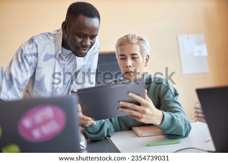 Confident Asian male student with tablet explaining his classmate data on screen