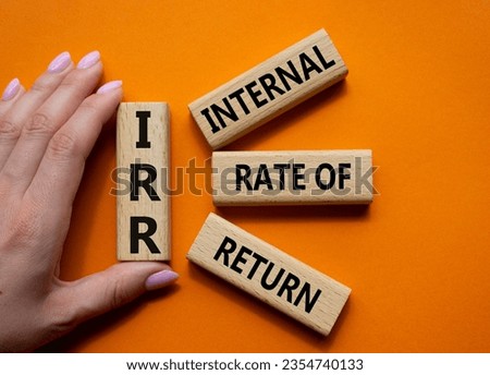 IRR - Internal Rate of Return symbol. Concept word IRR on wooden cubes. Businessman hand. Beautiful orange background. Business and IRR concept. Copy space.