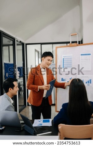 The boss stands near the board with graphs, demonstrates statistics, various personnel attending the training, introduces the new products of the company, in modern office

