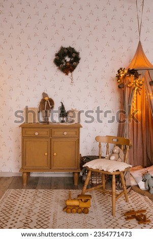 Interior of a children's room decorated for Christmas. A tent with toys and pillows, a Christmas tree, a wardrobe and a chair in beige tones
