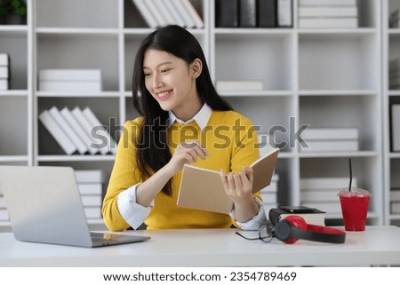 Happy Asian female student doing homework and doing academic studies in university library.