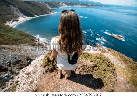 Edge of wonder: Standing at the cliff's brink, she embraces the serenity of the paradisiacal beachscape. Royalty-Free Stock Photo #2354795307