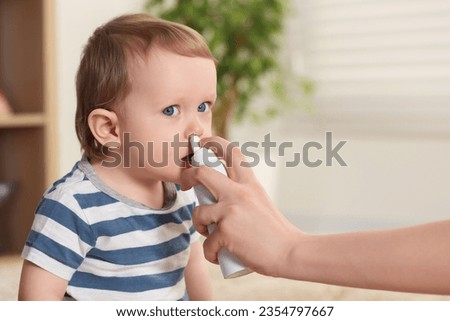Mother helping her baby to use nasal spray indoors Royalty-Free Stock Photo #2354797667