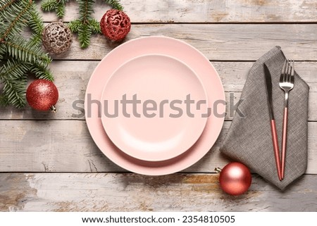 Festive table setting with pink plates, cutlery, Christmas balls and fir tree branches on grey wooden background