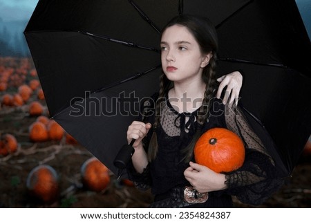 Halloween: Girl with a pumpkin and a black umbrella in her hands in a pumpkin field