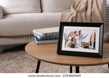 Frame with family photo and stack of books on wooden coffee table in room, space for text