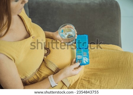 Prenatal Vitamins. Portrait Of Beautiful Smiling Pregnant Woman Holding Pill Box and a glass of water, Taking Supplements For Healthy Pregnancy While Sitting On Couch At Home, Free Space Royalty-Free Stock Photo #2354843755