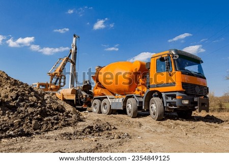 Mixer truck is in process of transshipment at building site. Pouring fresh concrete over ramp to truck with pump machine. Royalty-Free Stock Photo #2354849125