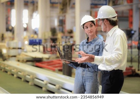 Young Beautiful engineer holding a laptop Standing and discussing with a senior male manager engineer wearing a white hardhat to solve problems in the production line in machinery in industrial plants Royalty-Free Stock Photo #2354856949