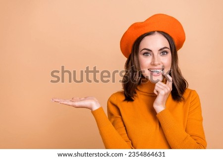 Portrait of pretty positive girl finger touch lips arm palm hold empty space isolated on beige color background