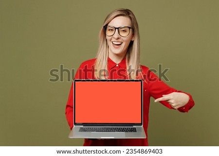 Young happy IT woman wears red shirt casual clothes glasses hold use work point finger on laptop pc computer with blank screen workspace area isolated on plain pastel green background studio portrait