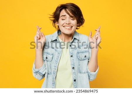 Young worried woman wear green t-shirt denim shirt casual clothes waiting for special moment, keeping fingers crossed, making wish, eyes closed isolated on plain yellow background. Lifestyle concept