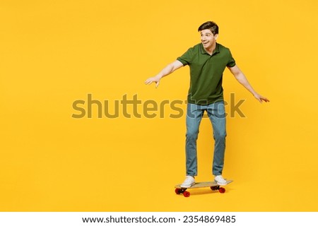 Full body side profile view caucasian active young happy man he wears green t-shirt casual clothes riding skateboard pennyboard isolated on plain yellow background studio portrait. Lifestyle concept