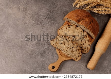 Freshly baked homemade bread, whole grain sourdough bread with a crispy crust, sliced and ears of rye and wheat on a concrete background with space for text, modern baking concept