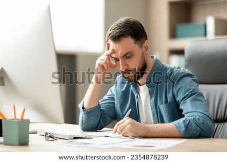 Focused young businessman sitting at desk in office and writing in notepad, handsome millennial male entrepreneur taking notes to notebook at workplace, ceo guy checking agenda, closeup Royalty-Free Stock Photo #2354878239