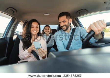 Car navigation app. Happy woman showing gps application on cellphone to driver man, family travelling and navigating vehicle with gadget, enjoying weekend trip