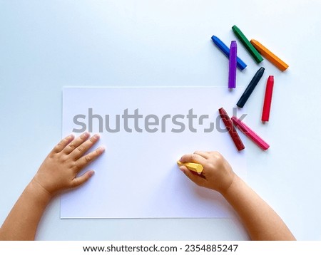 Childrens hands draw with colored wax crayons on a white sheet of paper. Top Royalty-Free Stock Photo #2354885247
