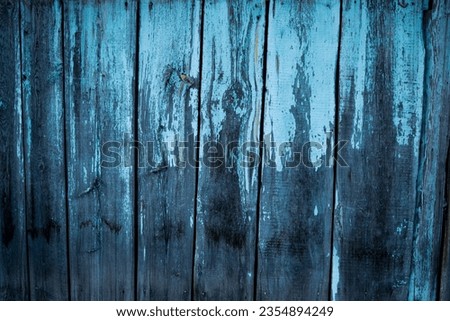 An old, shabby wooden fence, painted blue.  The blue paint cracked and crumbled from the wooden surface of the fence