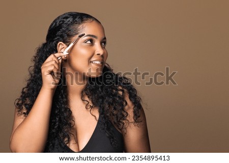 Eyebrow makeup. Latin plus size woman shaping brows with eyebrow brush, modeling brows or combing, looking aside at free space on brown background