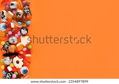 Halloween orange background with copy space on right, assorted sweets on left: traditional eyeballs chocolates, jelly worms, gummy ghosts. Happy Halloween holiday sale and trick-or-treat concept.