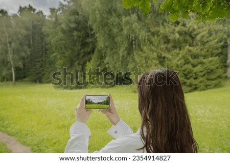 Back view portrait of a woman taking photo of a landscape with a smart phone in park in summer