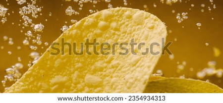 Deep fried potato chips under golden oil water. Frying rounded potatoes chip with hot boiling oil bubbles. Fast food and snack. Underwater cooking oily french fries or potatos chips in oils background Royalty-Free Stock Photo #2354934313