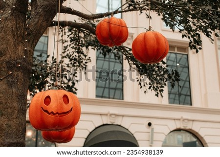 Bright pumpkin with a scary Halloween face hanging on a tree with garlands. Background for holiday poster