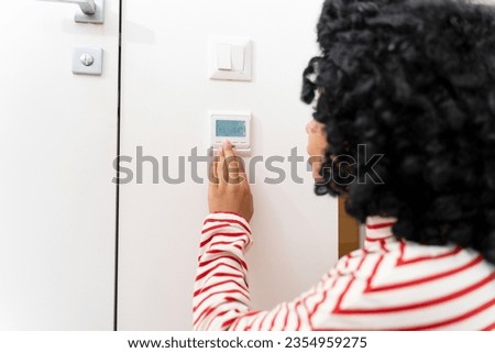 Curly African American standing in living room using smart home control panel, adjusting temperature. Smart house system concept
