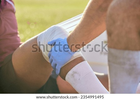 First aid, sport injury bandage and hands on knee with soccer accident, fitness and massage on a field. Training, workout and physical therapy of leg pain at game with emergency from exercise Royalty-Free Stock Photo #2354991495