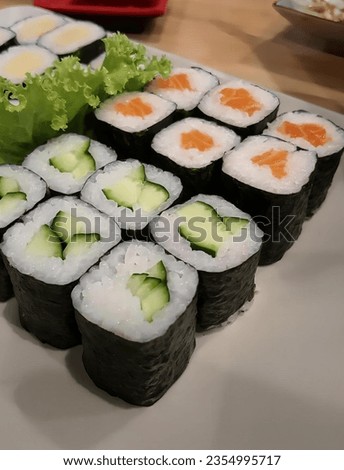 a photography of a plate of sushi with cucumbers and lettuce, plate of sushi rolls with cucumber and lettuce on top.