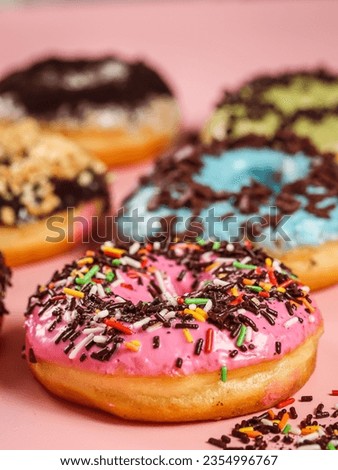 Ring doughnuts covered in icing and sprinkes with pastel pink background