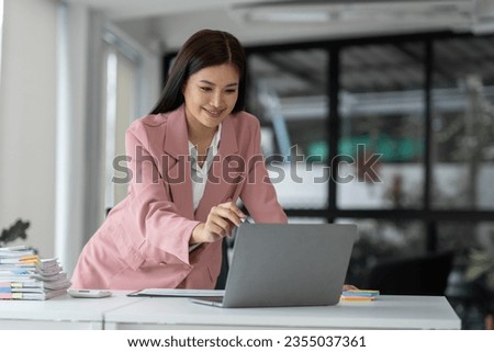 Young Asian businesswoman in casual suit happy smile While in modern office room with laptop about work in business administration, finance, accounting, marketing