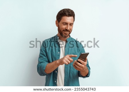 Smiling man in casual clothes use his mobile phone while standing on white background
