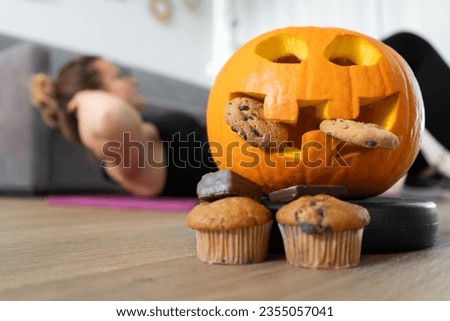 Woman exercising at home. Focus on Halloween pumpkin decoration and chocolate sweets. Healthy fitness lifestyle, seasonal fit diet choice. Rejecting unhealthy food. Sport workout and training concept. Royalty-Free Stock Photo #2355057041