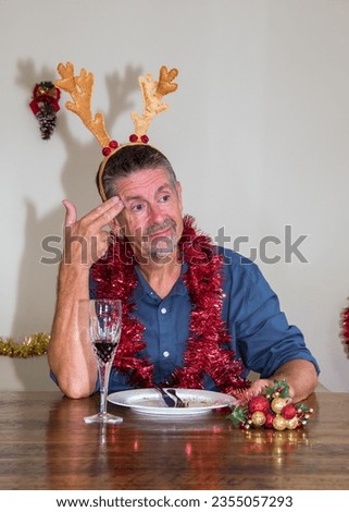 Christmas picture of boredom as a man comically displays his apathy towards Christmas. A bored and uninterested pose. An anti-Christmas image. Selective focus on the mans face. Unhappy Christmas.