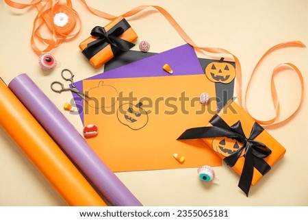 Gift boxes with Halloween decorations, candies and wrapping paper on beige background