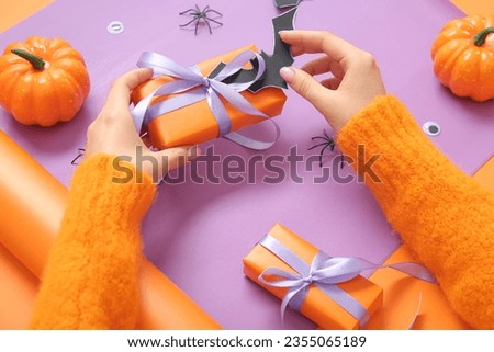 Woman with decorations wrapping gift boxes for Halloween on purple background