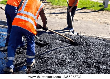 Road workers laying asphalt with shovels on street on summer day. Repair and restoration of road surface. Royalty-Free Stock Photo #2355068733