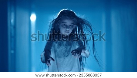 Little caucasian girl in ghost white sundress costume for halloween party creepily staring at camera while mystique wind blows her hair 