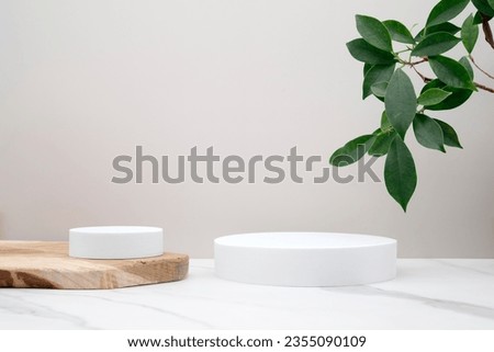 Circular podium for product presentation. Wooden and white marble surface. Photo studio, minimal and modern. Green plant and leaves on the side of the image. Royalty-Free Stock Photo #2355090109