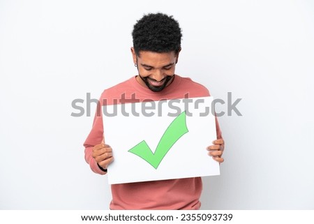 Young Brazilian man isolated on white background holding a placard with text Green check mark icon