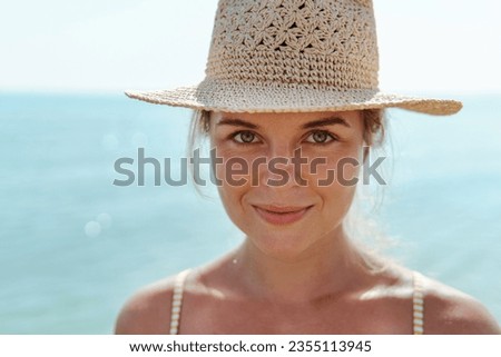 Woman radiates summer vibes wearing yellow striped bikini and a straw hat, enjoying her time on the beach.