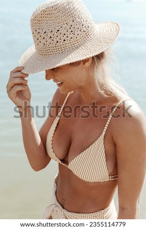 Woman radiates summer vibes wearing yellow striped bikini and a straw hat, enjoying her time on the sandy beach.