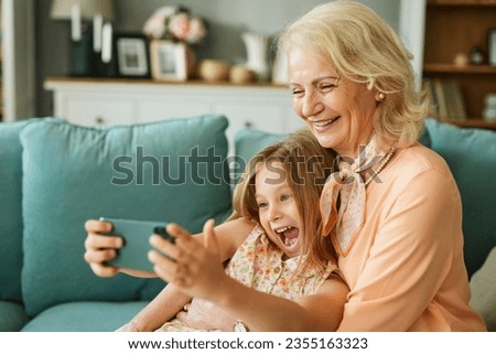 Happy grandmother and granddaughter taking selfie using smartphone in the living room