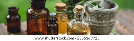 Concept of alternative herbal medicine. Bottles of tincture or potion, organic essential oils, healthy herbs, floral extracts on wooden table. Pure natural ingredients for cosmetic production banner