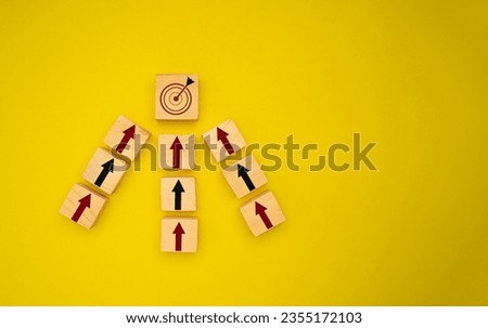 Focus on a goal and achieve a successful business concept. Wooden cubes with red and black arrows pointing to the dartboard icon are on a yellow background. Top view. Business and planning concept