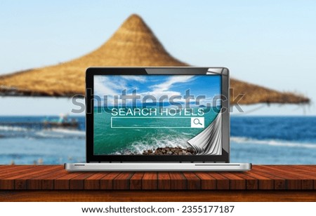 Search hotels website on laptop computer screen, a straw beach umbrella and tropical beach on background. Online booking concept.